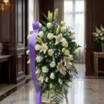 Pedestal fúnebre Salvación con rosas blancas, lirios y follaje verde, presentado en una sala de velación premium con luz natu