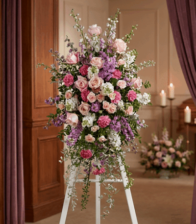 Pedestal funerario 'Luz de Elisa' con rosas, claveles y lirios en tonos pastel, realzado en una sala de velación con iluminac