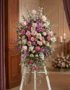 Pedestal funerario 'Luz de Elisa' con rosas, claveles y lirios en tonos pastel, realzado en una sala de velación con iluminac