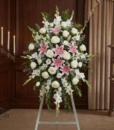 Pedestal floral funerario "El Legado de Josafat" con lirios rosas, rosas blancas y gladiolos en sala de velación elegante.
