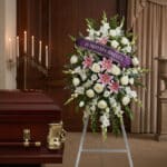 Pedestal floral "El Legado de Josafat" con rosas blancas, lirios rosados y gladiolos, cinta morada "En Profunda Simpatía" jun