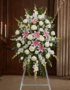 Pedestal floral funerario "El Legado de Josafat" con lirios rosas, rosas blancas y gladiolos en sala de velación elegante.