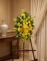 Pedestal de homenaje "El Legado de Sebastian" con un arreglo floral fúnebre de lirios y crisantemos amarillos, presentado ele