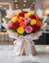 Ramillete o bouquet de 18 rosas multicolor (rojas, amarillas, naranjas, rosas) con empaque coreano elegante sobre mesa de már