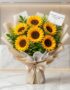 Ramillete de seis girasoles grandes y vibrantes con follaje verde, envuelto en papel coreano beige y blanco con un lazo de sa