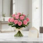 Ramillete de rosas rosadas frescas sobre mármol blanco, con tarjeta de regalo y cinta satinada, listo para entregar.