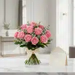 Ramillete de rosas rosadas frescas sobre mármol blanco, con tarjeta de regalo y cinta satinada, listo para entregar.