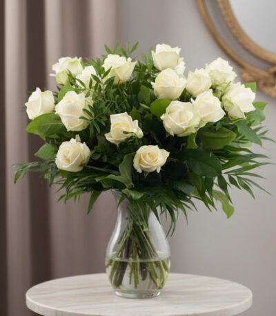Ramo de 18 rosas blancas frescas en un jarrón de cristal, con follaje verde, sobre una mesa de mármol y fondo elegante.