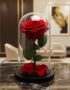Rosa preservada roja en cúpula de cristal sobre una mesa de mármol negro, con un fondo elegante de lobby de hotel boutique.