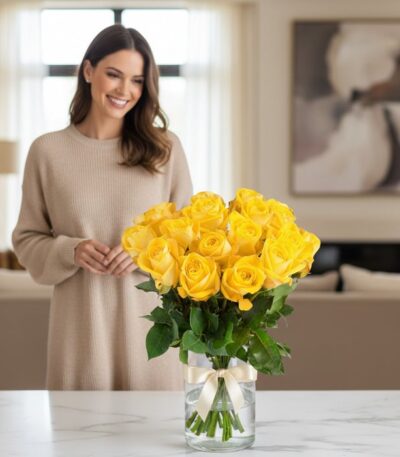 Mujer sonriente admirando un arreglo floral de 18 rosas amarillas en un jarrón de cristal con lazo, en un hogar de diseño luj