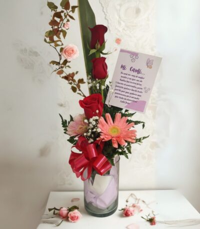 Arreglo floral Solitario Pienso en Ti con rosas rojas, gerberas y follaje en un jarrón de cristal, sobre un fondo elegante de