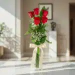 Solitario de cinco rosas rojas Marilyn en un jarrón de cristal con lazo satinado, sobre mármol pulido en un ambiente luminoso