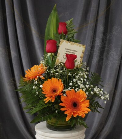 Arreglo floral 'Solitario Tu Recuerdo' con tres rosas rojas, tres gerberas naranjas, follaje verde y flores blancas pequeñas,